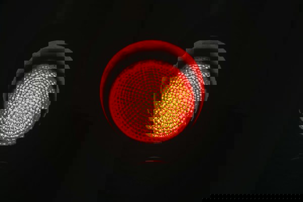 A close-up of a red traffic light illuminated against a dark background.